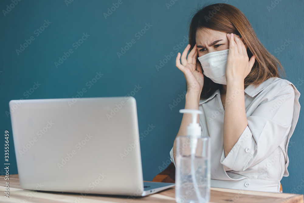 A beautiful businessman in a white dress with a mask and has a severe headache while working on a laptop in the office Alcohol gel placed on her desk A beautiful businessman in a white dress with a mask and has a severe headache while working on a laptop in the office Alcohol gel placed on her desk