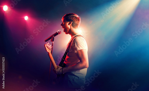 Young male singer performing on a stage and playing the guitar