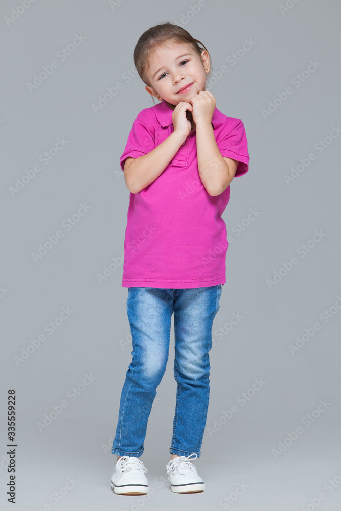 Full length portrait of funny active little girl wearing casual clothes: jeans and pink t-shirt isolated on grey studio background Full length portrait of funny active little girl wearing casual clothes: jeans and pink t-shirt isolated on grey studio background