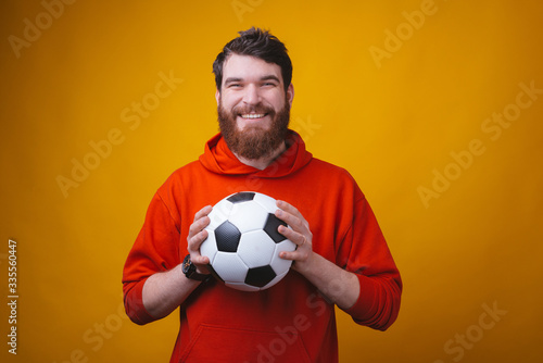 Photo of smiling man is holding a football or soccer ball and showing thumb up or like gesture.