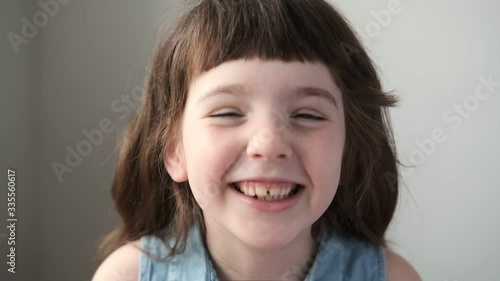 A 6-7 year old girl looks at the camera and laughs. Close up.