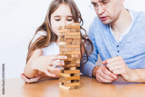 Girl and dad play a game at home, cost a tower of blocks, cubes, jenga, puzzle for brain development, mental intelligence, child development, school, home, quarantine, vacation, time with family