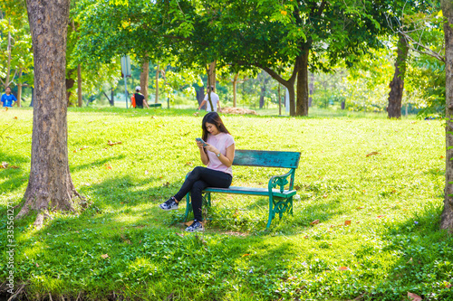Beautiful asian women use smartphone sitting on bench in city green park © themorningglory