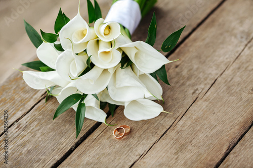 Wedding rings and a bouquet of the bride lie on wooden boards.