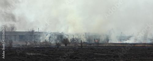 Fototapeta Naklejka Na Ścianę i Meble -  Fire on abandoned farm, panoramic view through the smoke on the ashes rural barns