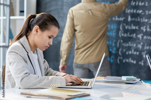 Pretty girl sitting by desk in front of laptop while preparing presentation