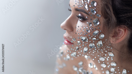Fantastic fashion portrait of a young beautiful woman with transparent crystals on her face and shoulders.