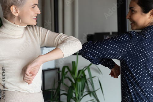 Focus on happy young female mixed race friendly colleagues bumping elbows, avoid handshaking hugs while greeting each other in office, preventing coronavirus infection spread, social distance concept. photo