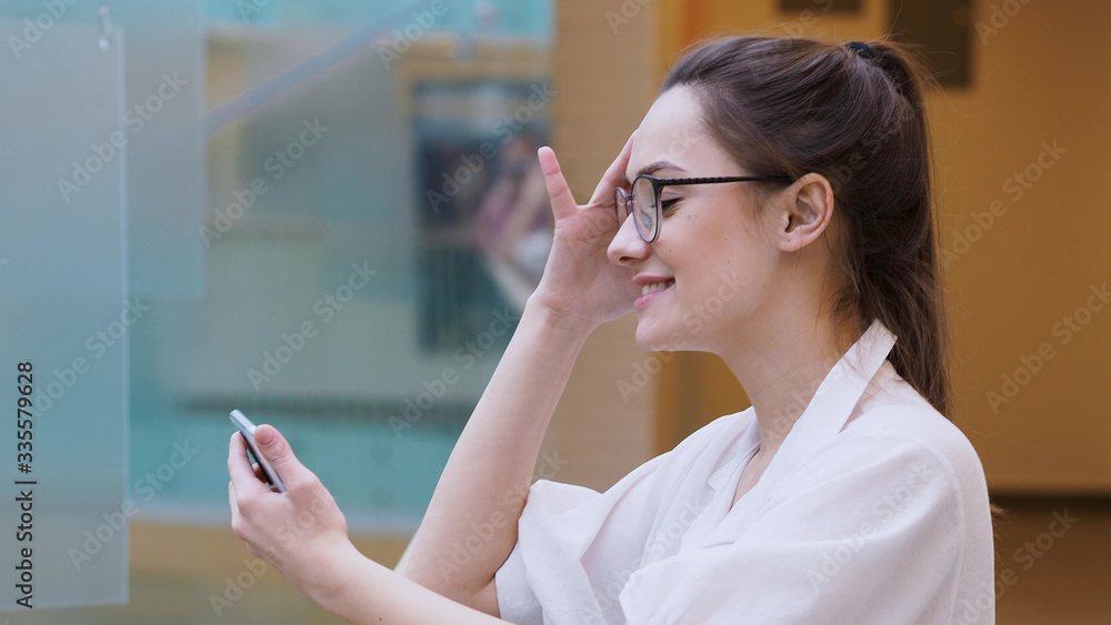 young business lady uses a smartphone. surprised girl in white shirt and glasses makes a phone call.
