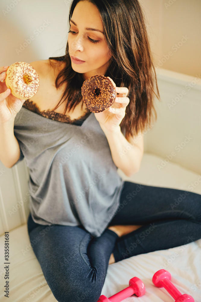 Pretty woman holding chocolate donuts and dumbbell. Food concept. Pretty woman holding chocolate donuts and dumbbell. Food concept.