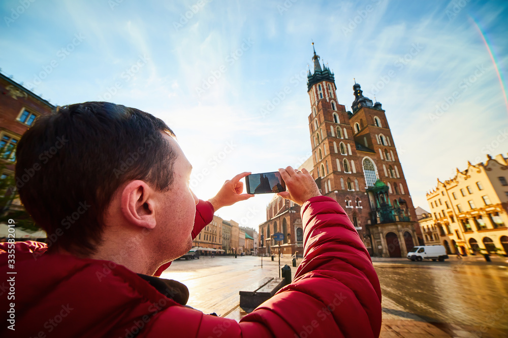 Obraz premium Young man tourist making photo of the famous St. Mary's Basilica on the Market square during the sunrise in Krakow, Poland