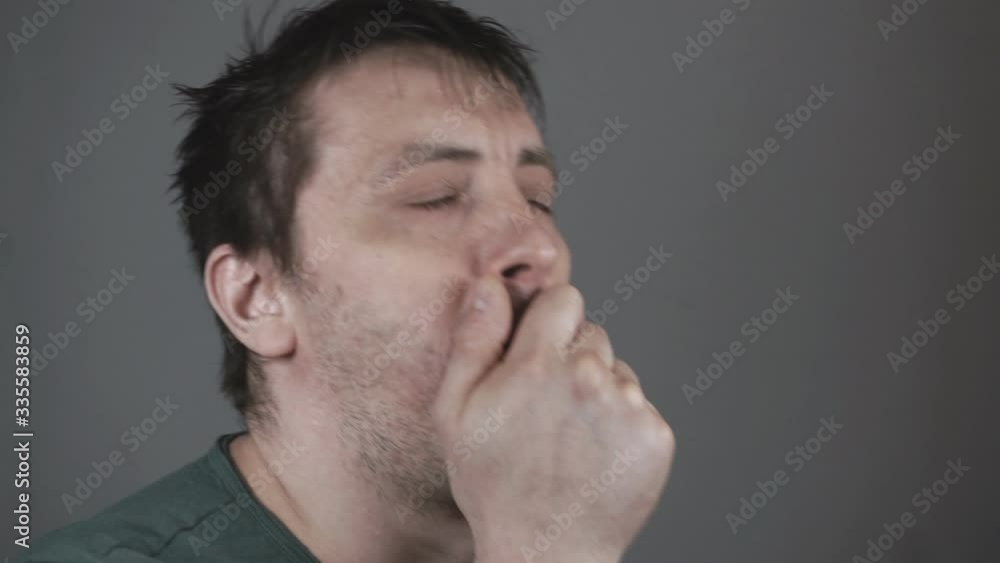 A young man coughs, covering his mouth with his hand. A young man coughs, covering his mouth with his hand.