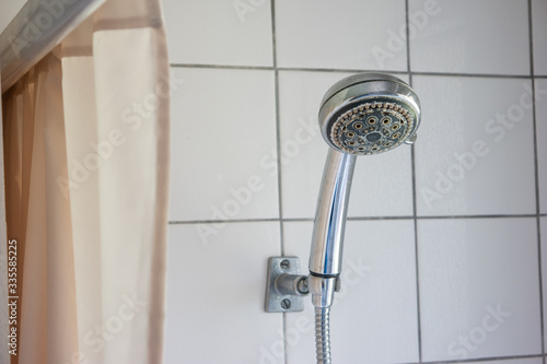 Dirty corroded limescale calcified shower head hanging from a stand inside cabin visible curtain photo