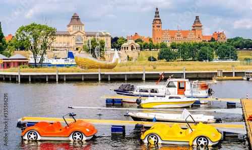 Pedalos and boats docked on Rampart of Brave embankment of Odra River. National Museum, Regional Authority and Passport Office in background, Szczecin