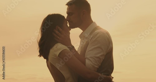 Couple embracing man kissing woman. Tender groom stroking bride's face in sunlight with hands touching face. Real-time, hand-held shot, close up, 4K.