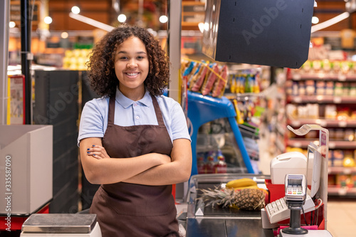 Foto Pretty young smiling African-american female sales clerk looking at you