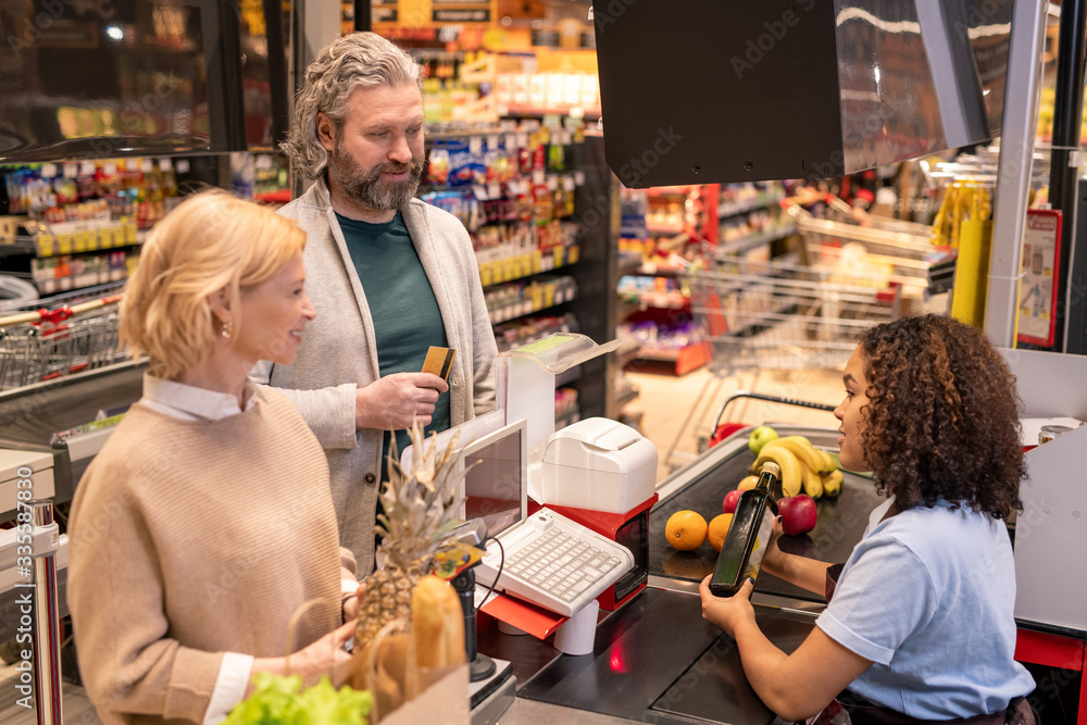 Young cashier scanning bottle of olive oil while looking at mature couple