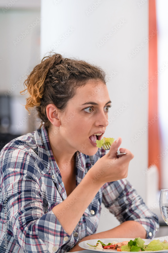 A woman with brown hair, dressed in a checkered shirt eating salad with a fork. diet concept. A woman with brown hair, dressed in a checkered shirt eating salad with a fork. diet concept.