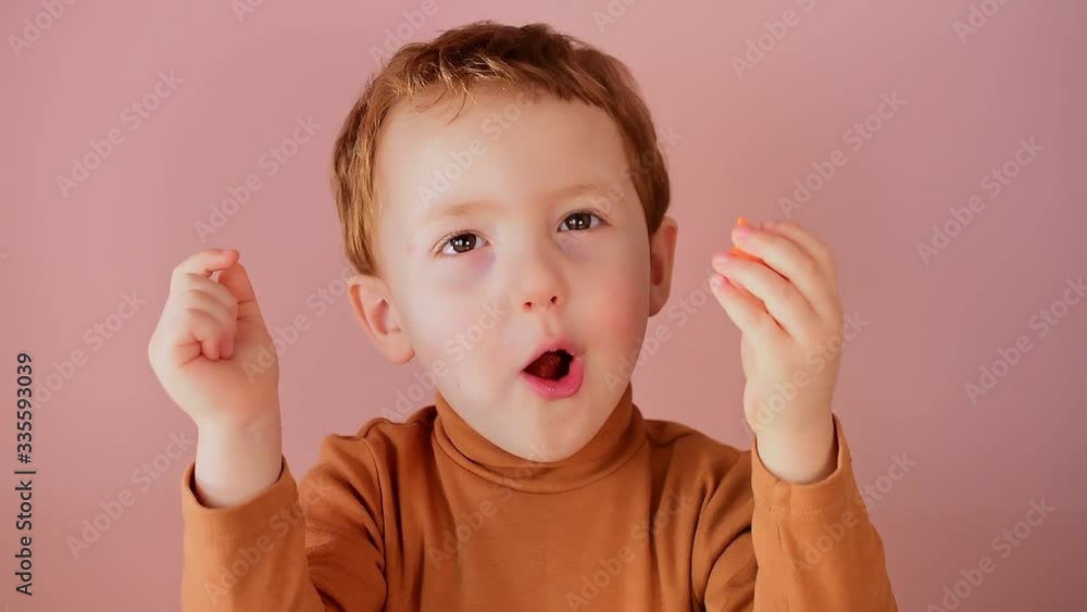 Cute little red-haired boy eats a carrot on a pink background Cute little red-haired boy eats a carrot on a pink background