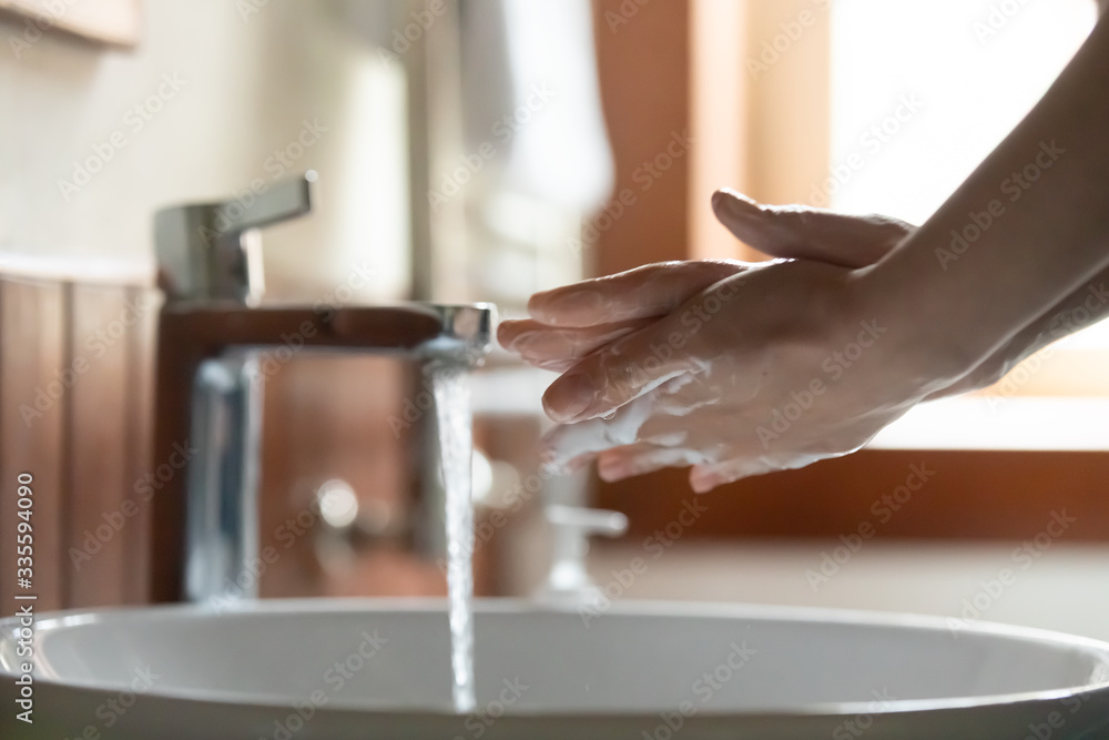 Side close up view focus on female washing carefully hands with bubbling soap, preventing spreading coronavirus. Cautious young woman doing healthcare skincare routine in bathroom after back home.