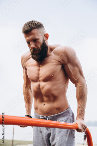 Strong muscular bearded man doing push-ups on uneven bars in outdoor street gym. Workout lifestyle concept.