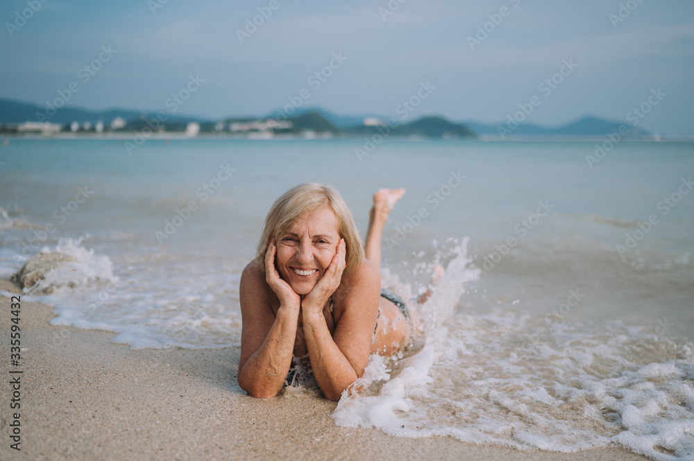 Happy smiling excited elderly senior woman tourist playing in water and swimming in the big waves on the ocean sea beach. Traveling along Asia, active lifestyle concept. Happy smiling excited elderly senior woman tourist playing in water and swimming in the big waves on the ocean sea beach. Traveling along Asia, active lifestyle concept.
