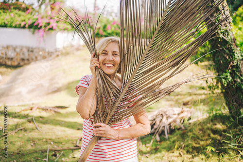 Senior european traveling active smiling woman tourist walking enjoying in Sanya tropical jungle. Traveling along Asia, active lifestyle concept. Discovering Hainan, China. Posing with palm branch