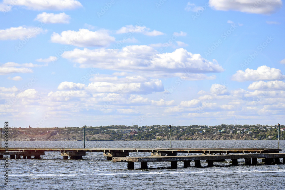 Pier made of concrete slabs against background of river and cloudy sky.