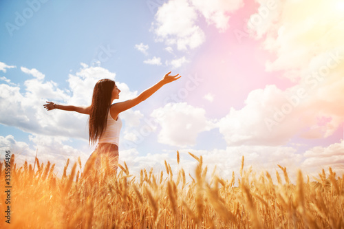 Happy woman enjoying the life in the field. Nature beauty, blue sky,white clouds and field with golden wheat. Outdoor lifestyle. Freedom concept. Woman jump in summer field