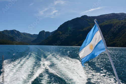 Bild auf Leinwand Argentine flag on the back of boat with lake and mountains and sky in background