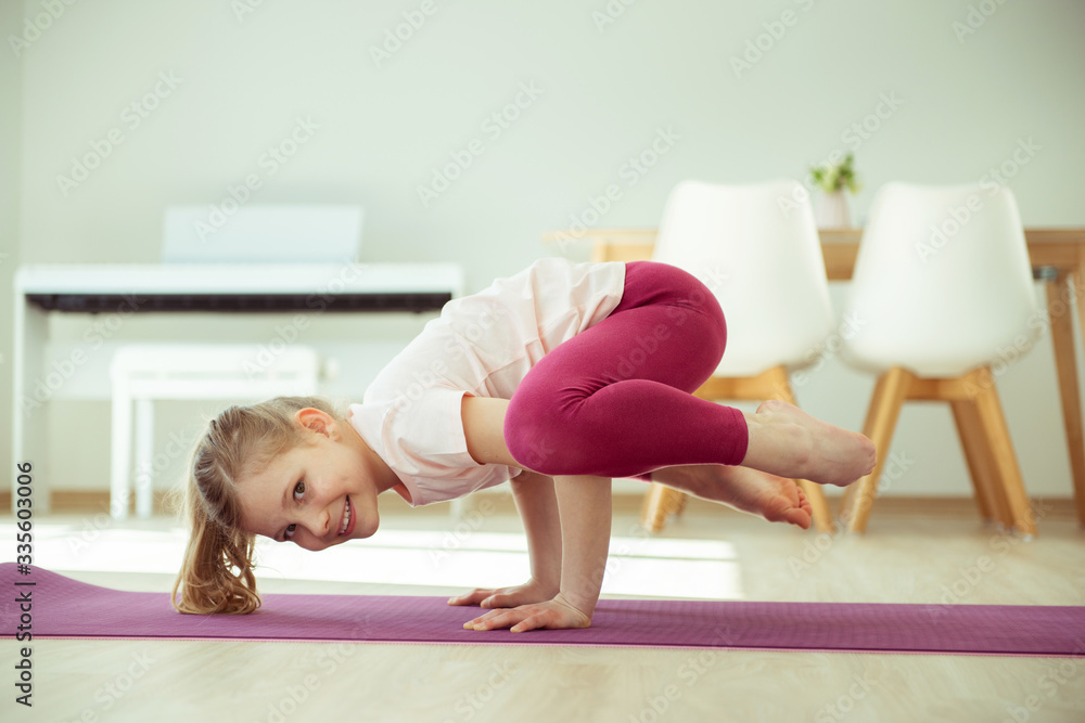 Pretty happy child girl making yoga exercises at home during coronavirus quarantine Pretty happy child girl making yoga exercises at home during coronavirus quarantine