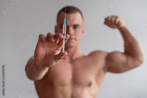 Attractive male bodybuilder with a naked torso holds a dope syringe. The athlete puts himself an injection of growth hormone.