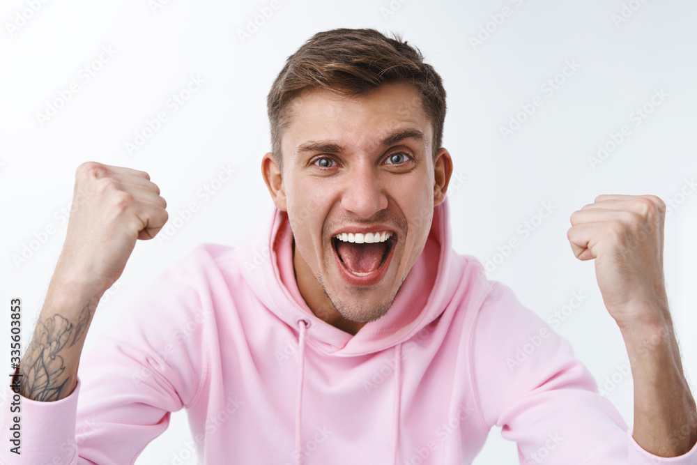 Close-up portrait of cheerful supportive young blond man, sport team fan cheering and chanting during competition, watching match online, raise hands up triumphing, winning, celebrate scored goal Close-up portrait of cheerful supportive young blond man, sport team fan cheering and chanting during competition, watching match online, raise hands up triumphing, winning, celebrate scored goal