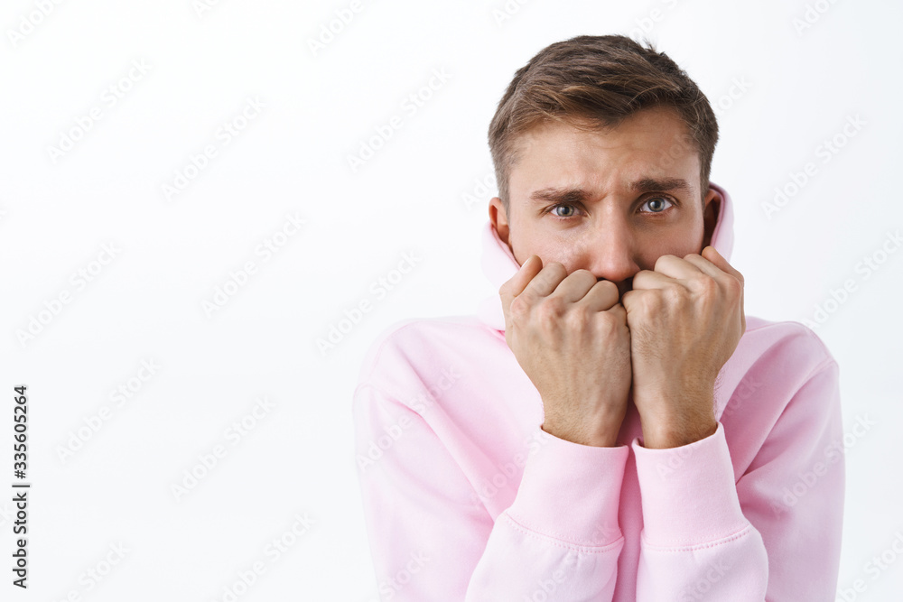 Portrait of young timid blond man, feeling insecure and scared, cover mouth and look scared eyes, trembling from fear, standing frightened over white background, watching horror movies Portrait of young timid blond man, feeling insecure and scared, cover mouth and look scared eyes, trembling from fear, standing frightened over white background, watching horror movies