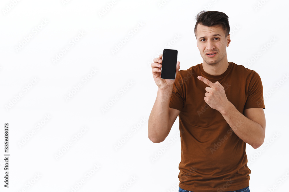 Skeptical and unimpressed caucasian italian guy in brown t-shirt, showing something bad on smartphone, pointing at mobile phone display judging awful webpage or social media photo, white background Skeptical and unimpressed caucasian italian guy in brown t-shirt, showing something bad on smartphone, pointing at mobile phone display judging awful webpage or social media photo, white background