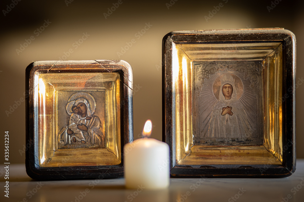A candle burning in front of an icon of holy mother and child