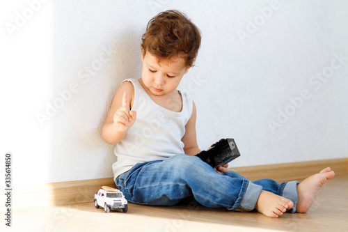 a little boy on the floor plays cars I am dressed in a white T-shirt and jeans, A bright white room and sunlight