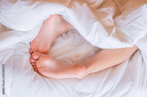 Child feet under the white blanket. Tenderness of morning dream