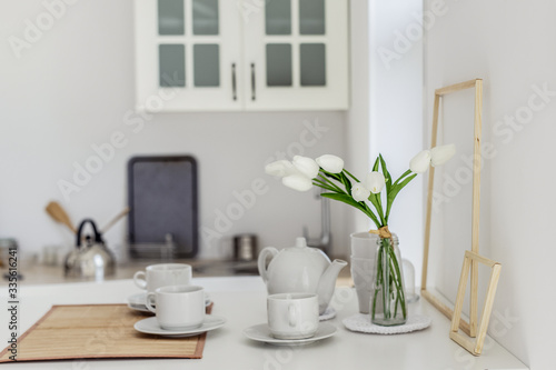 White tulips in a glass vase on a white table. In a light interior in a Scandinavian style, minimalism.