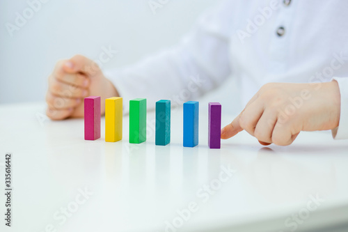 Building items in a single row. Concept of diagnostics of children's autism. A child plays with a colored wooden construction tool. Close.
