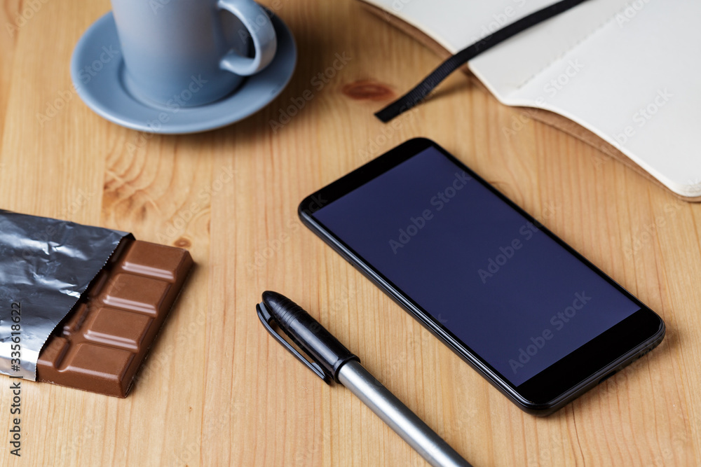Mesa de trabalho com xicara de cafe, caneta, smartphone e barra de chocolate Mesa de trabalho com xicara de cafe, caneta, smartphone e barra de chocolate
