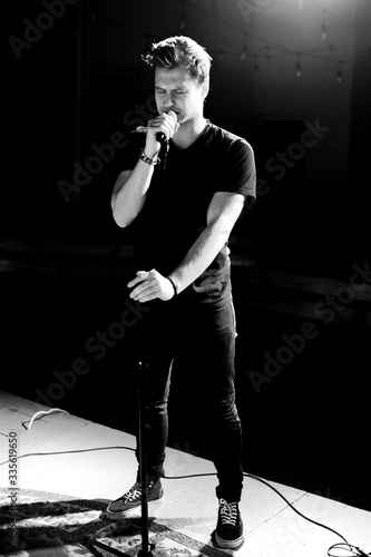 Young handsome guy emotionally sings and speaks into the microphone. Black and white photography