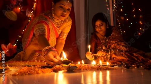 Two beautiful Indian Bengali women in Indian traditional dress lightening diyas/lamps in the floor in light bokeh background on Diwali evening. Indian lifestyle and Diwali celebration