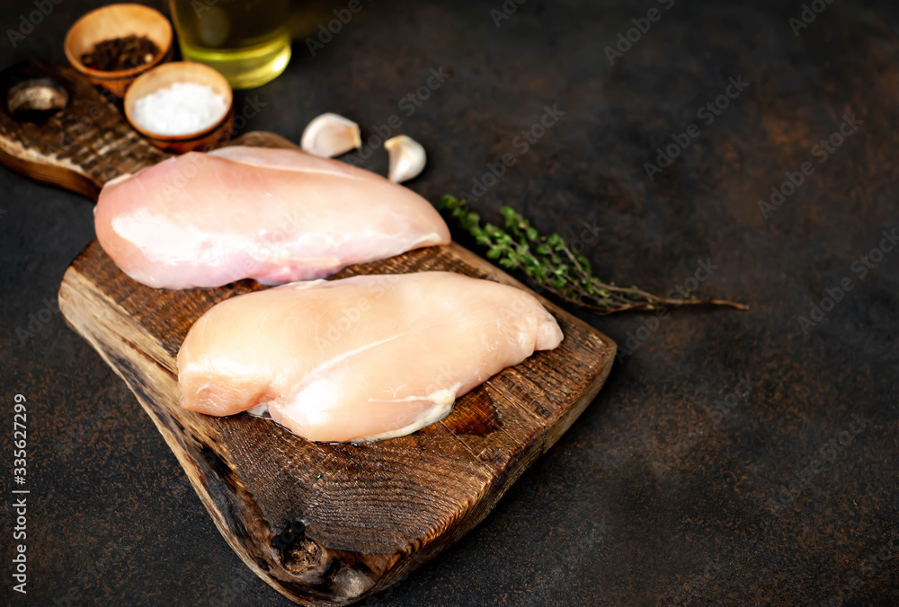raw chicken breast on a cutting board with spices and a meat knife on a stone background 
with copy space for your text