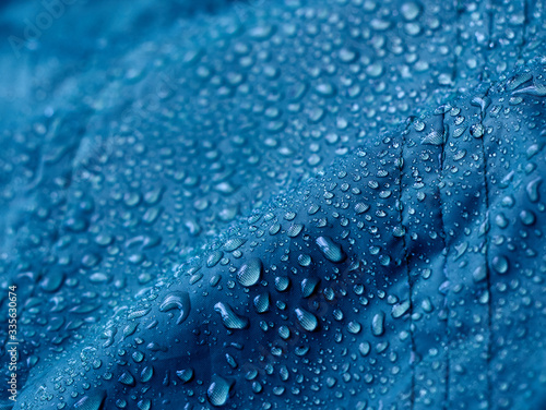 Rain water droplets on blue fiber waterproof fabric. Blue background.