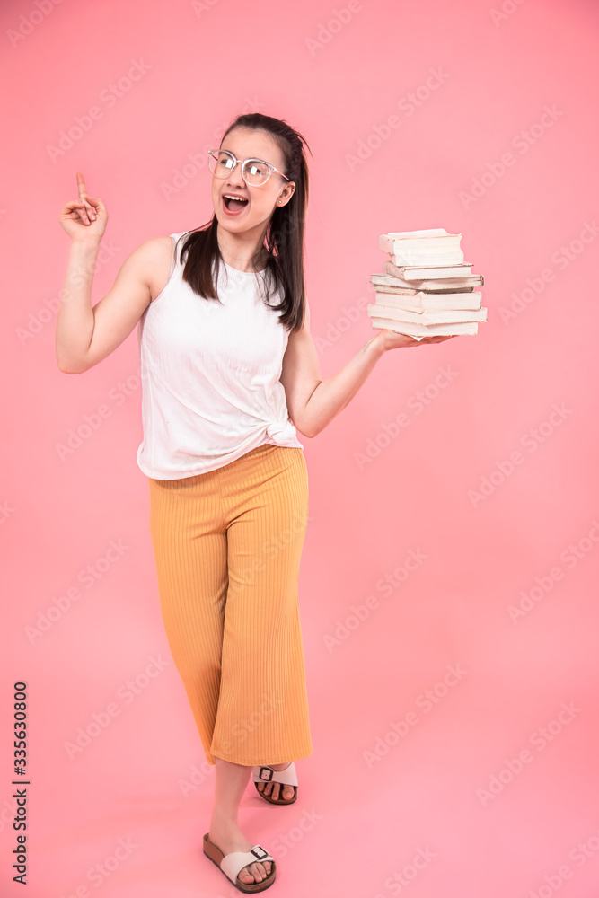Portrait of a young woman with glasses on a pink background with books in her hands . Portrait of a young woman with glasses on a pink background with books in her hands .