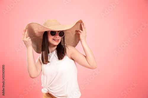 Portrait of a young woman in a summer hat and glasses, on a pink background .