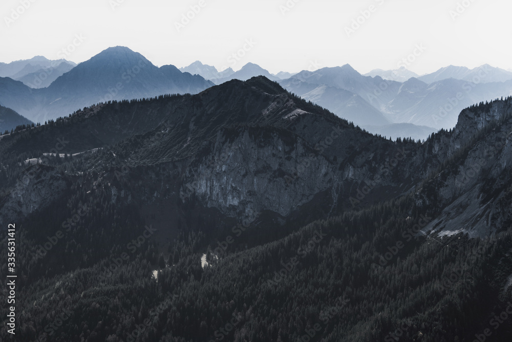 Wonderful landscape of mountain ranges and peaks. A view of the misty slopes, silhouette, and layers mountains at distance. Misty coniferous forest hills. Travel background. Vintage toning effect.