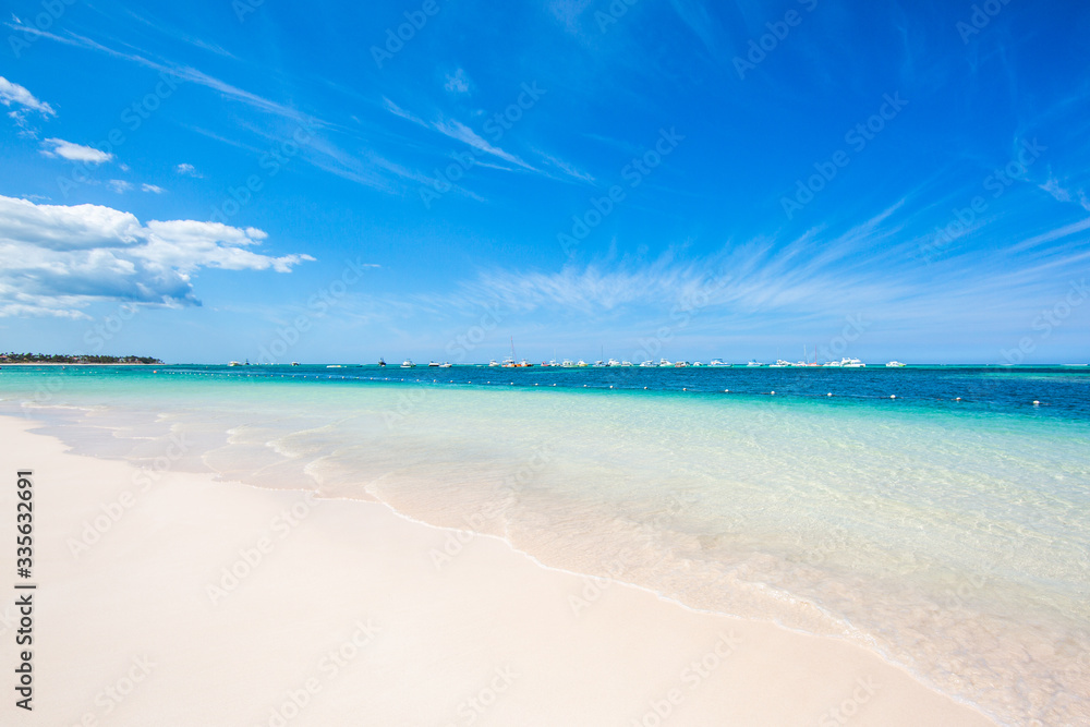 Waves on white sand on the shore of the Atlantic Ocean turquoise color of water and clear blue sky. Yachts and boats moored on the horizon. Caribbean, Punta Cana Dominican Republic