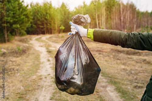 hand holds a bag with trash on the background of the forest. environmental cleaning concept photo